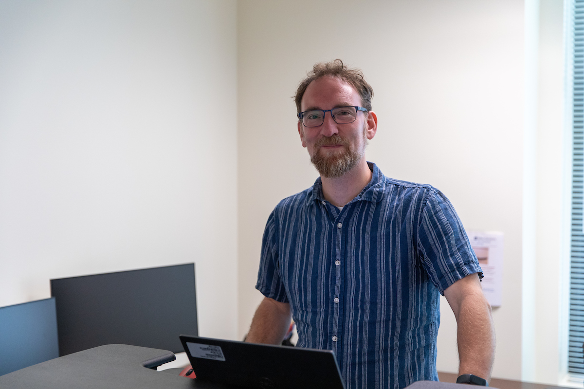 Nick Obis stands behind computer and desk