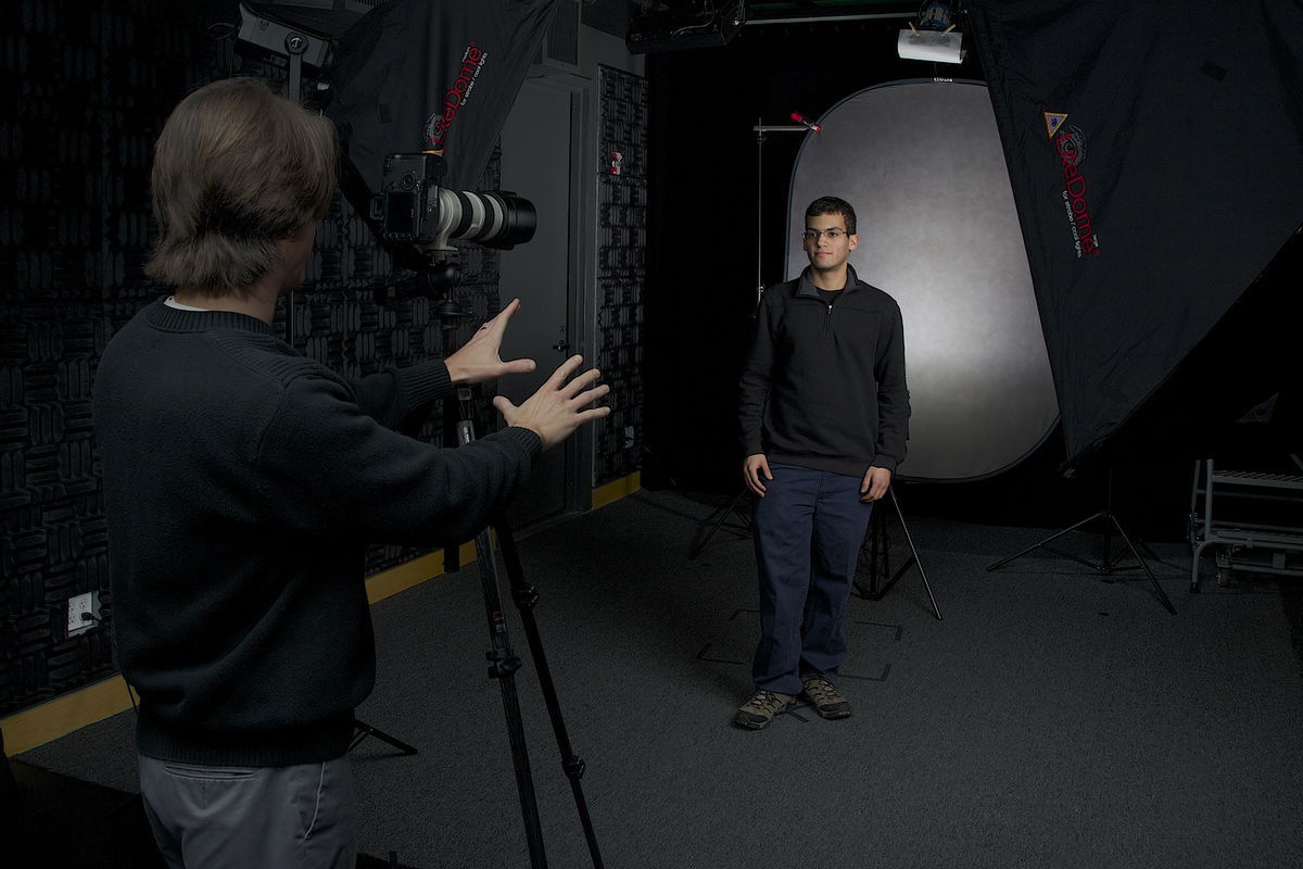 A photographer poses a subject in a darkened studio