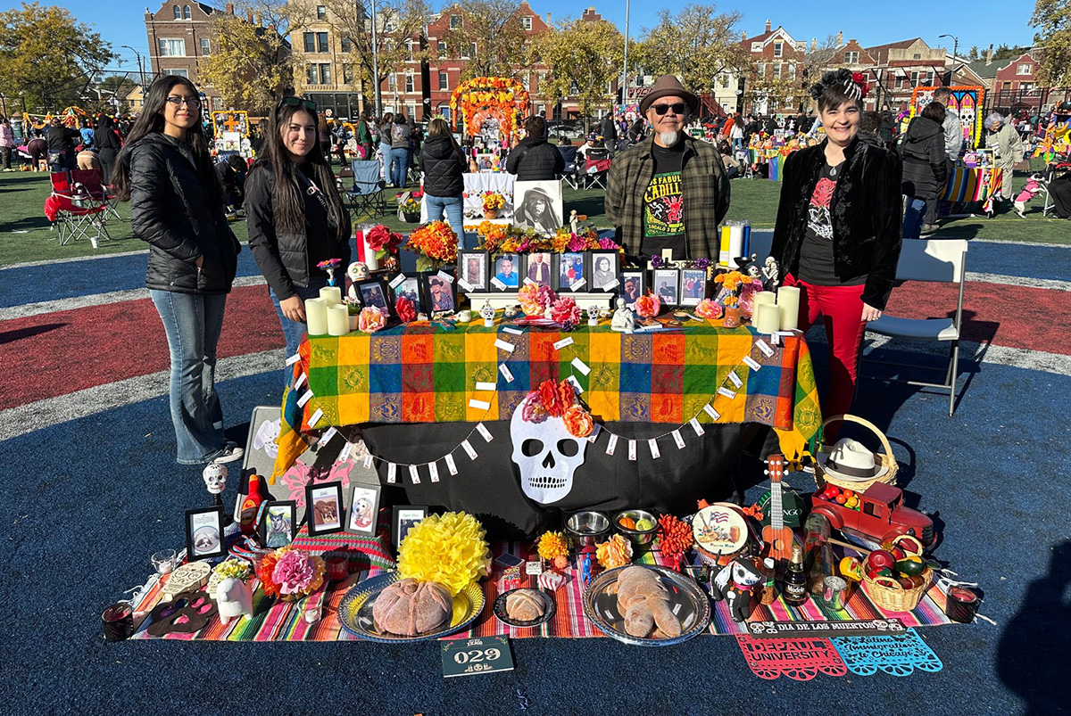 Four people stand behind a Día de los Muertos altar outdoors