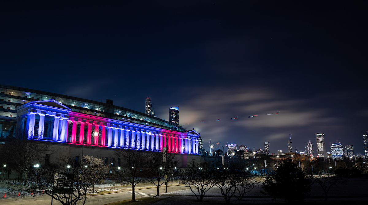 East entrance to Soldier Field, lit in blue and red, with the Chicago skyline in the distance