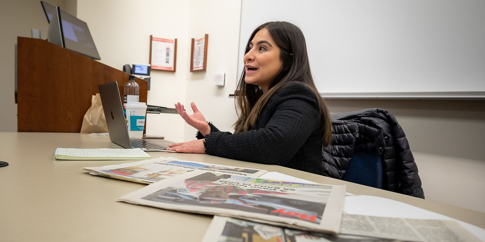 Laura Rodriguez teaches from the front of a classroom with newspapers spread in front of her