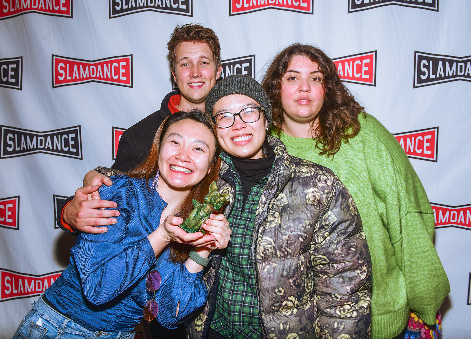 Four young people smiling and holding a statue award in front of a step and repeat that says 'Slamdance'