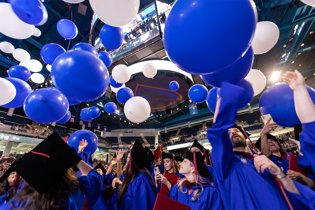 Graduates celebrate in a sea of blue and white balloons.