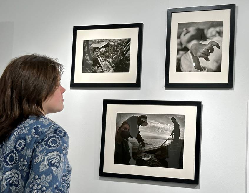 Student looking at 3 black and white photographs on a white wall. 