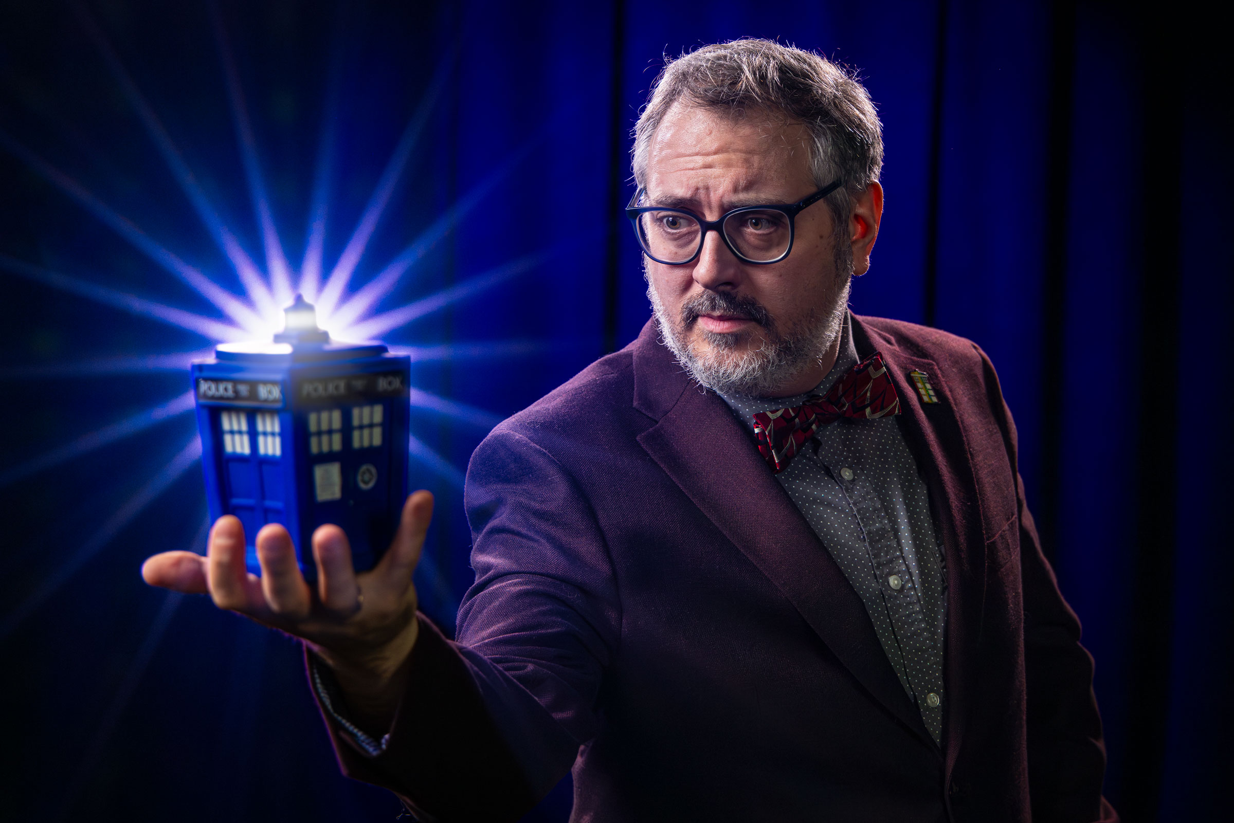 Paul Booth in a suit with a Tardis pin holding a little glowing tardis 