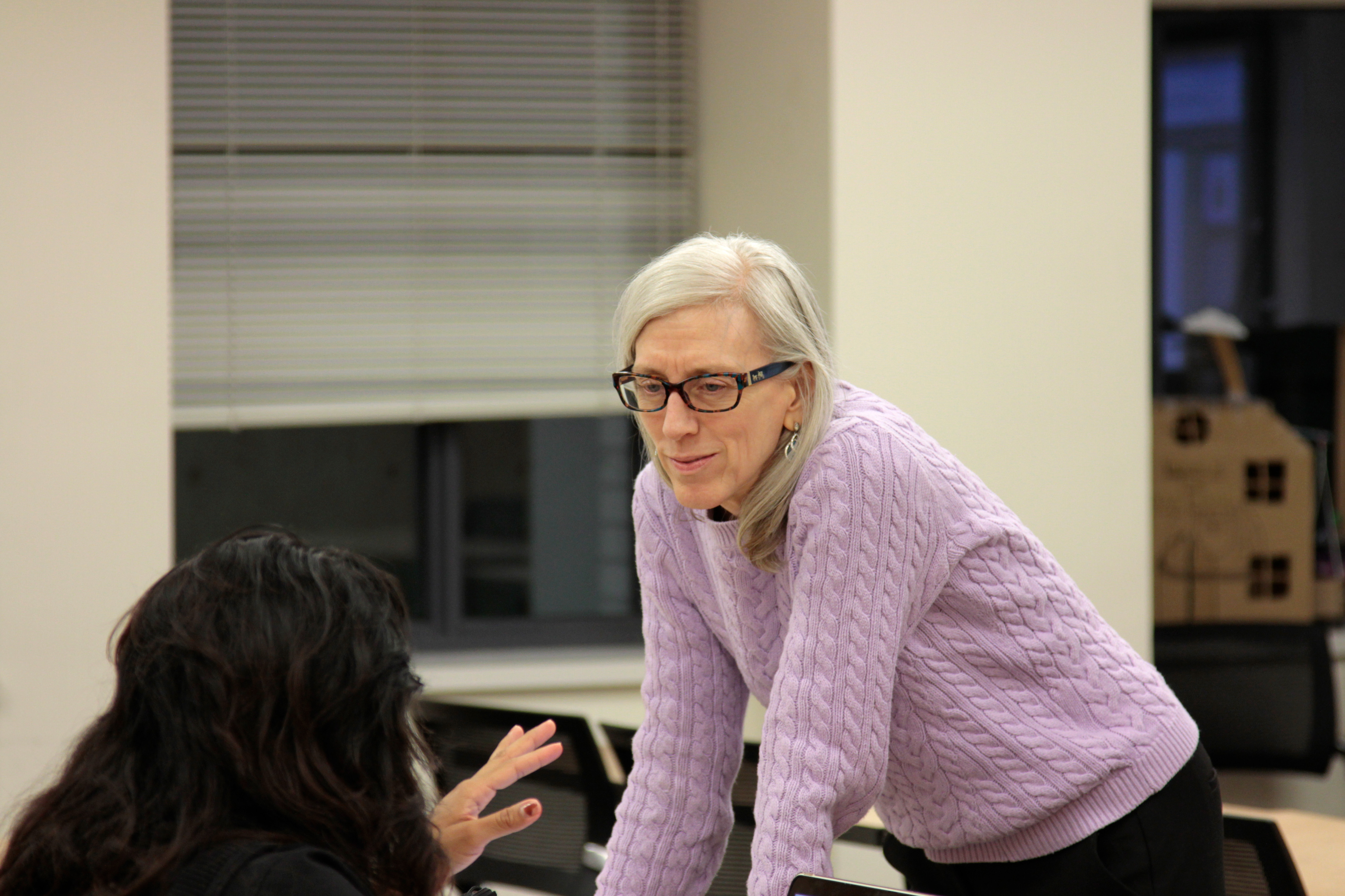 Professor leans on a table to speak to student at an ECE class. 