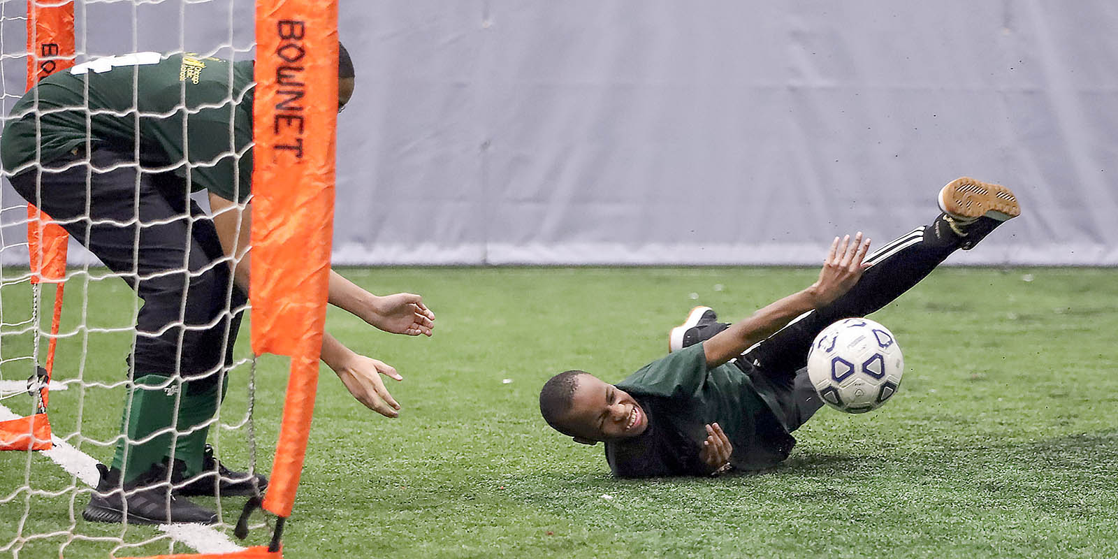 A Special Olympics athlete dives towards the soccer ball while the goalie waits behind him
