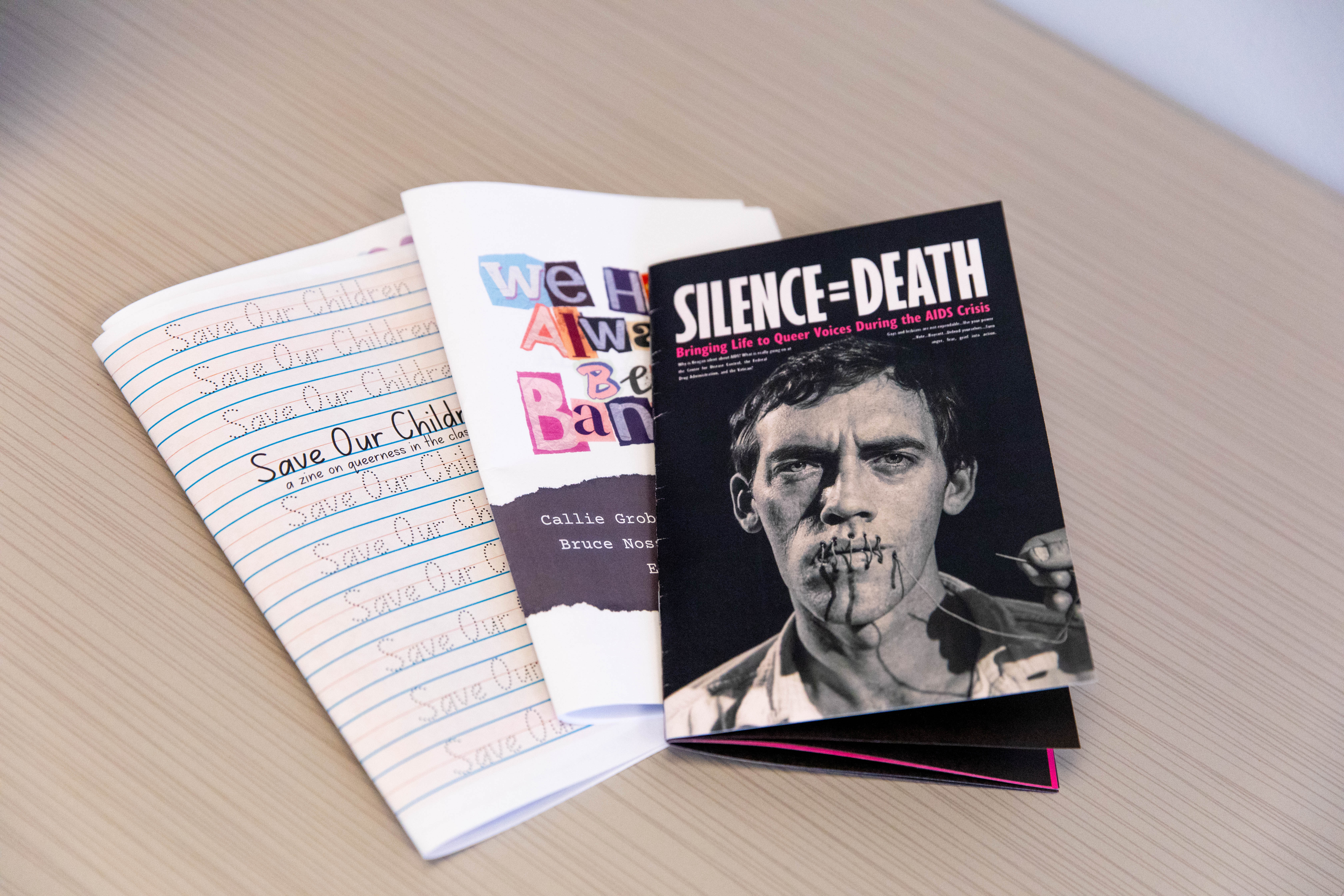 Three zines with the titles "Save Our Children," "We Have Always Been Banned" and "Silence=Death"