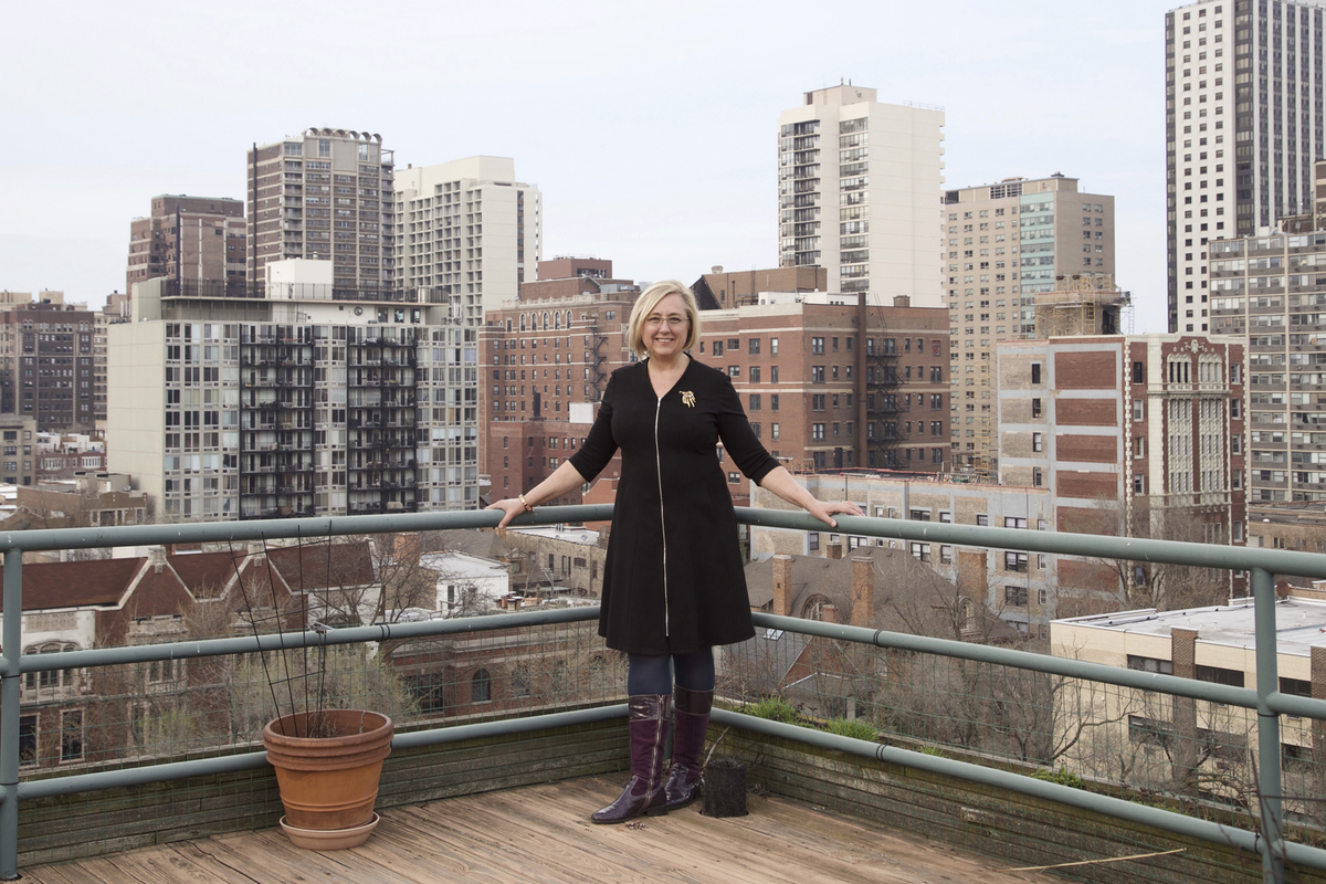 Barrie Jean Borich standing on a balcony, with a cityscape behind her