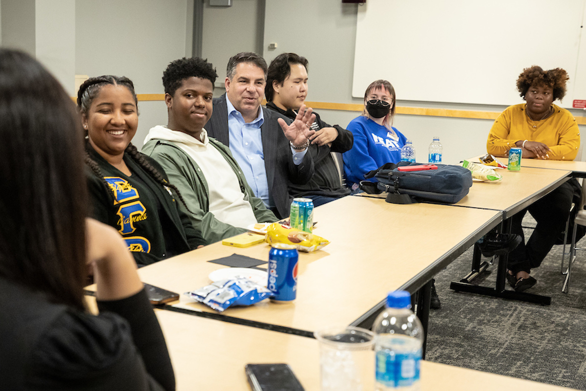 DePaul President Rob Manuel talks with student leaders, sitting alongside one another on the far side of a conference table.