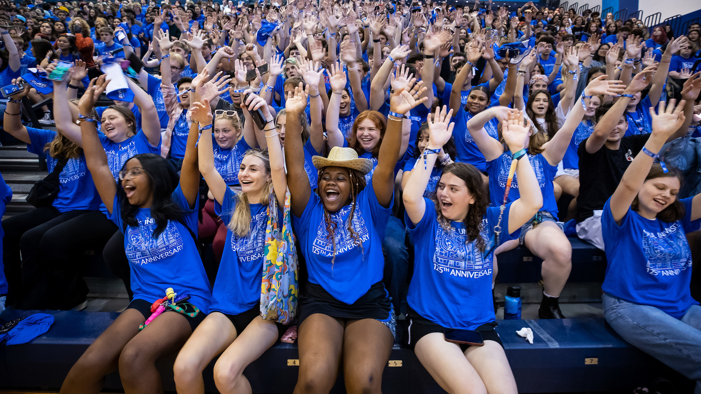 Students wearing blue shirts cheering in bleachers during Welcome event