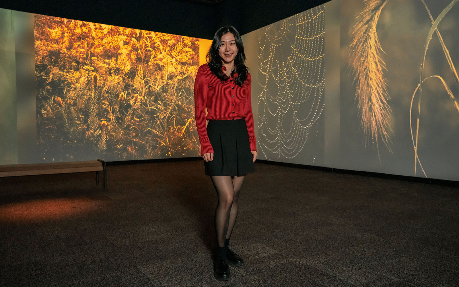 Yaxi Yang stands in front of a digital display of nature photos at the nature museum