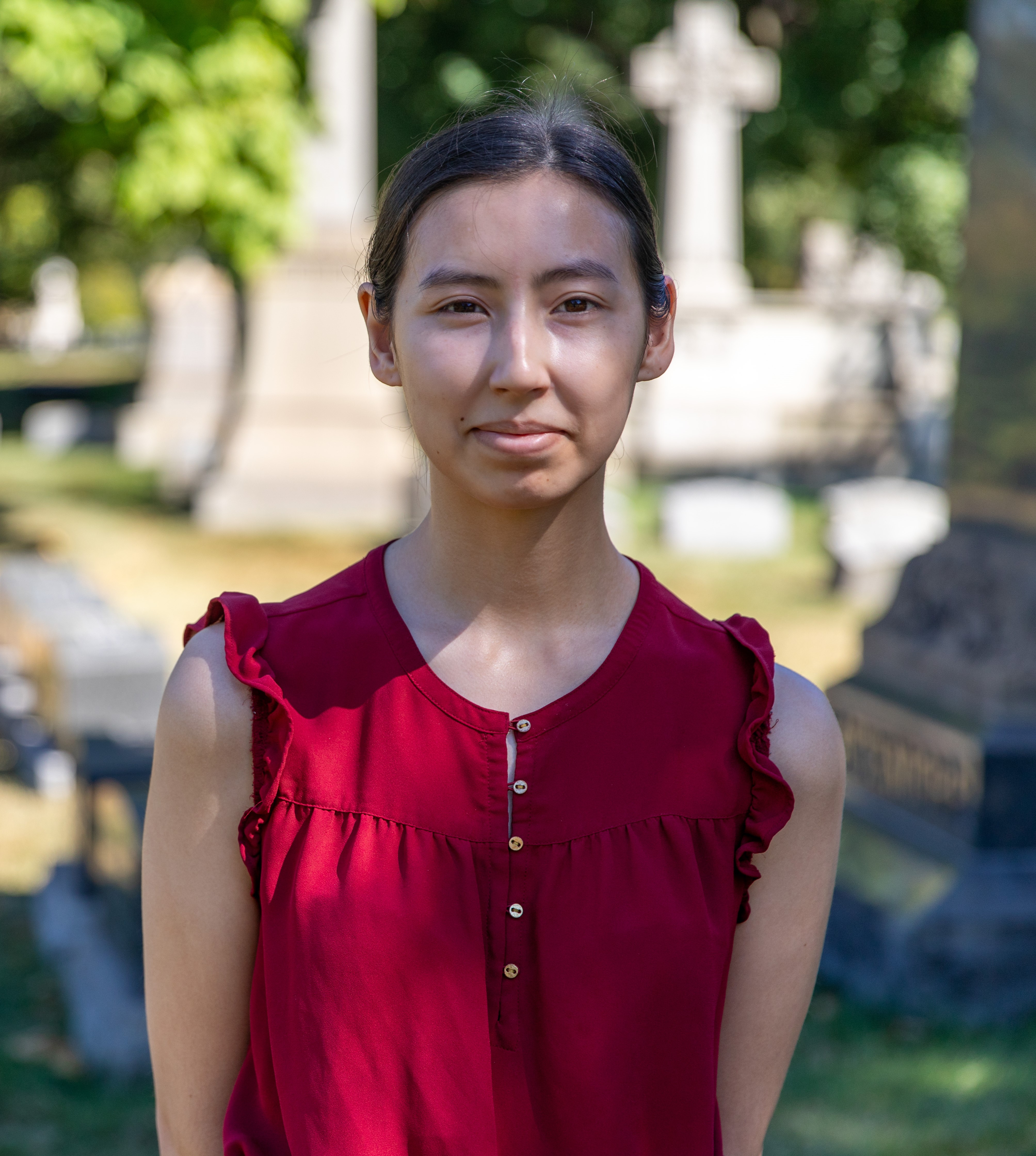 Misha Mikami is wearing a red shirt, standing in Graceland Cemetery.